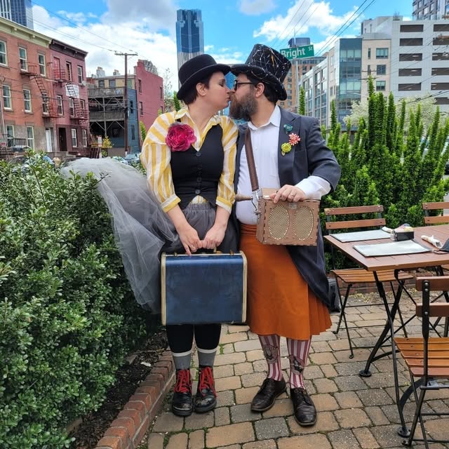 The Moobox duet in playful performance costumes, sharing a kiss with their music box.